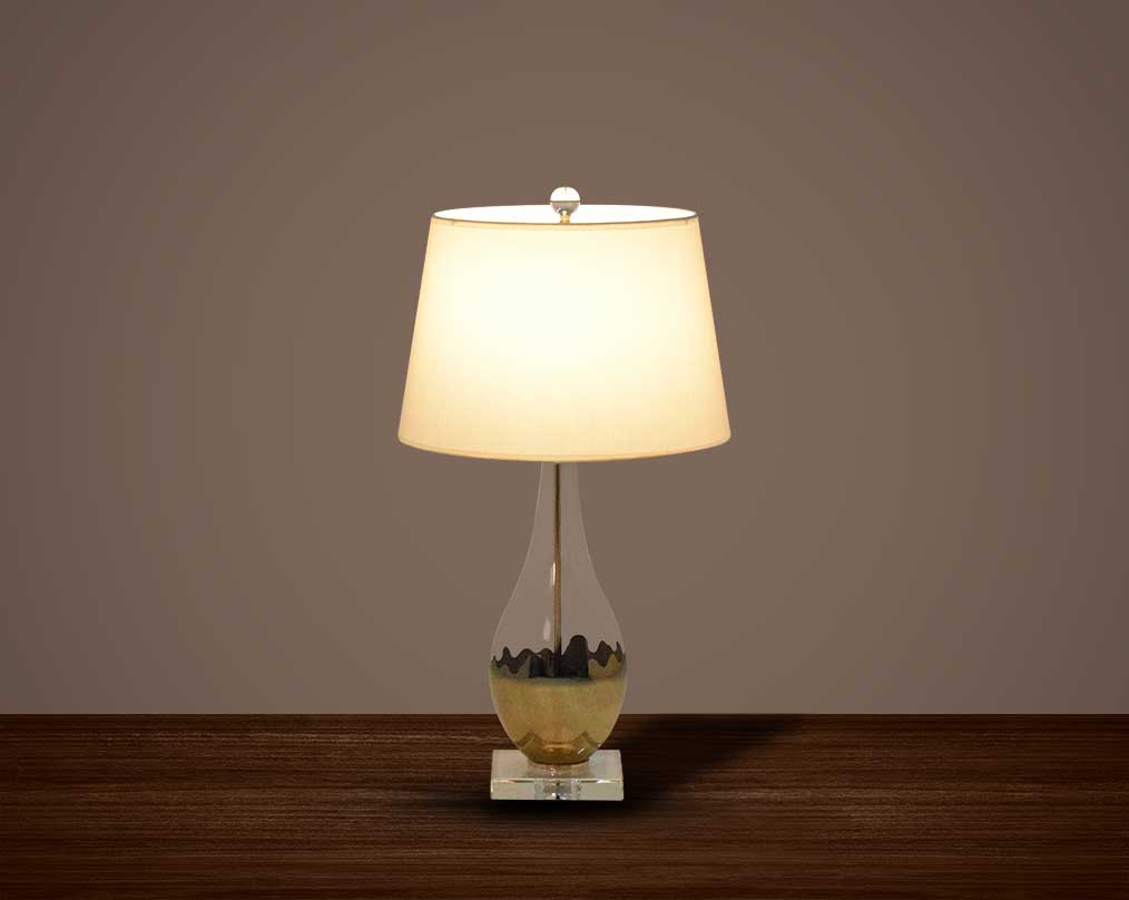 Table lamp with metallic gold and glass decorative base with translucent fabric shade.