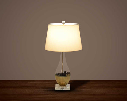 Table lamp with metallic gold and glass decorative base with translucent fabric shade.
