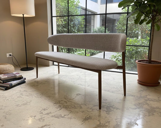 Beige bench in a modern living room with large windows and a plant.