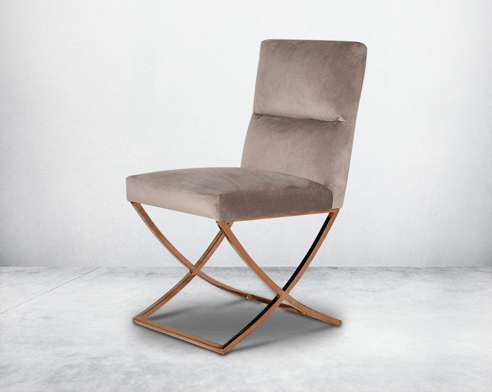 Dining chair upholstered in fabric with rose gold plated stainless steel legs in a cross design.