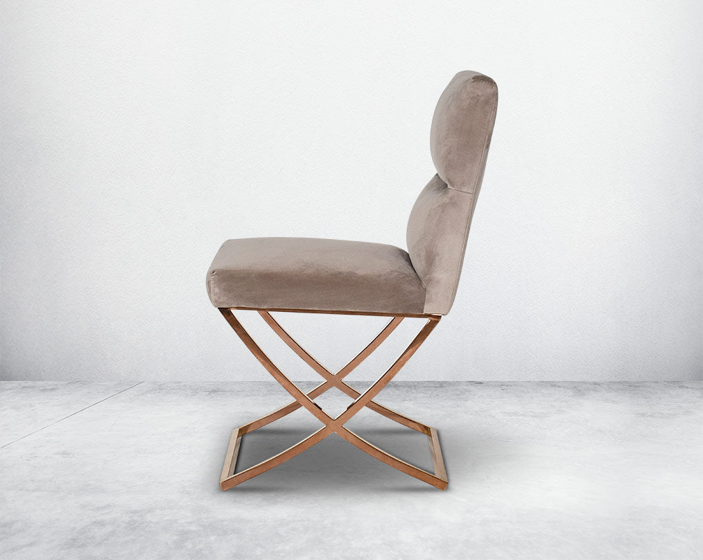 Dining chair upholstered in fabric with rose gold plated stainless steel legs in a cross design.