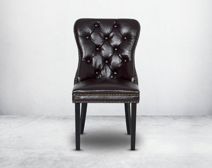 Dining chair upholstered in faux leather with front view buttoned tufted back the chair has antique gold rivets, legs in dark vintage brown wood.