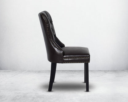Dining chair upholstered in faux leather with side view buttoned tufted back the chair has antique gold rivets, legs in dark vintage brown wood.