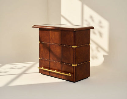Bar counter in distressed cognac leather with a vintage look with brass hardware and wooden slats.
