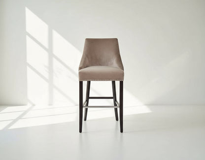 Bar chair upholstered in fabric with buttoned tufted back and silver rivets, the stool has a stainless steel front bar as a foot rest with legs in dark vintage brown wood front view 