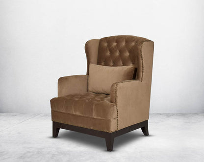 Wing arm chair upholstered in fabric and tufted with antique gold rivets on the arms and front with cushion and legs in brown oak side view