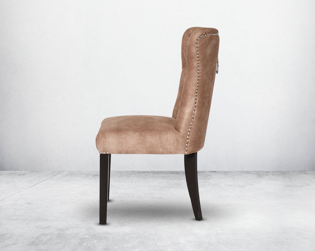 Dining chair upholstered in fabric with tufted back and birchwood legs. Stainless steel decorative ring at the back with stainless steel rivets on the sides.