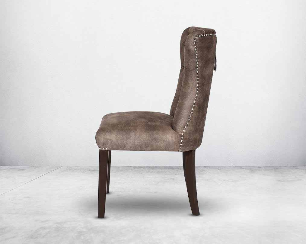 Dining chair upholstered in fabric with tufted back and birchwood legs. Stainless steel decorative ring at the back with stainless steel rivets on the sides.