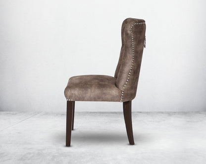 Dining chair upholstered in fabric with tufted back and birchwood legs. Stainless steel decorative ring at the back with stainless steel rivets on the sides.