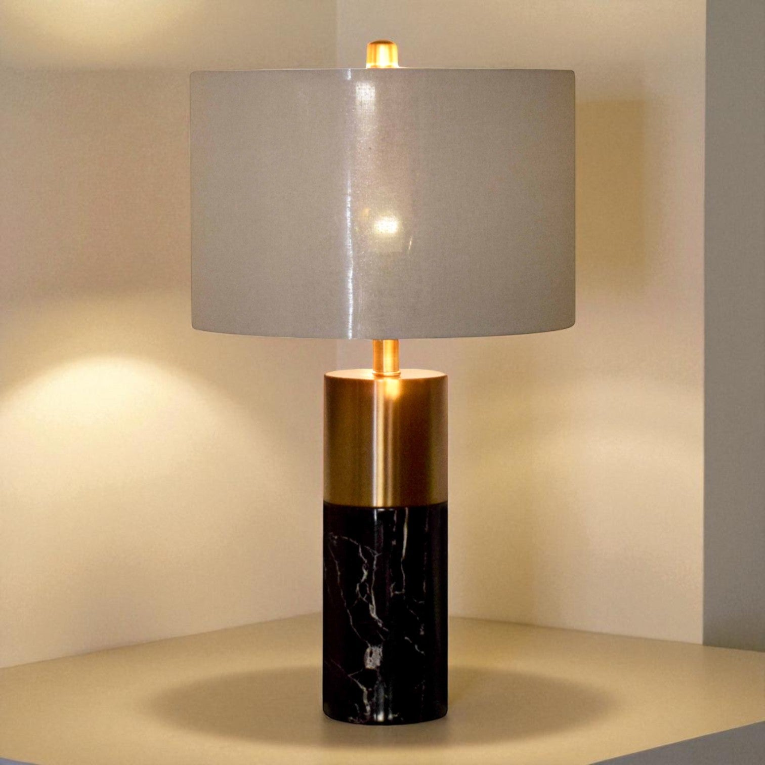 Table lamp with a gray shade and black base with gold accents on a neutral background