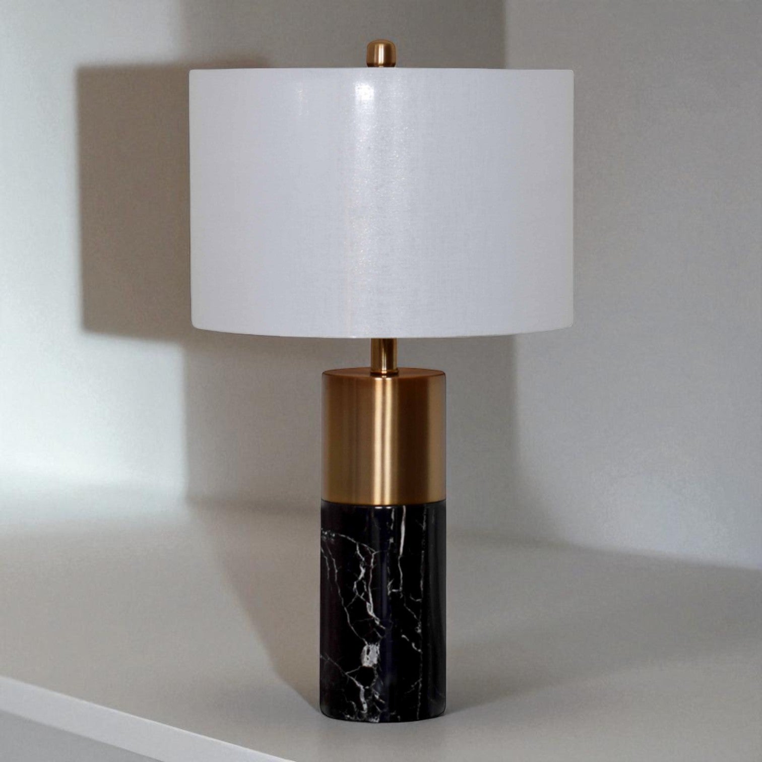 Table lamp with white shade, gold accent, and black marble base on a neutral background