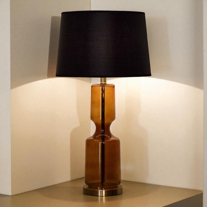Table lamp with a black shade and brown cylindrical base on a neutral background