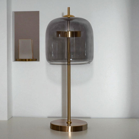 Table lamp with smoked glass shade and brass base on a neutral background