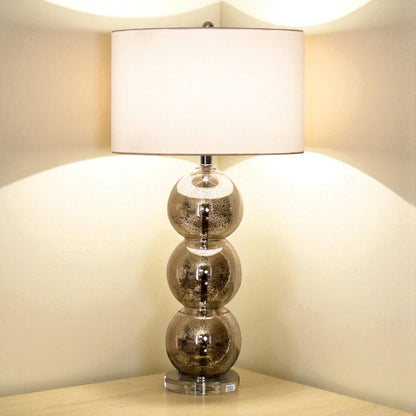 Table lamp with glass base and white shade on a wooden surface.