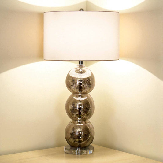 Table lamp with glass base and white shade on a wooden surface.