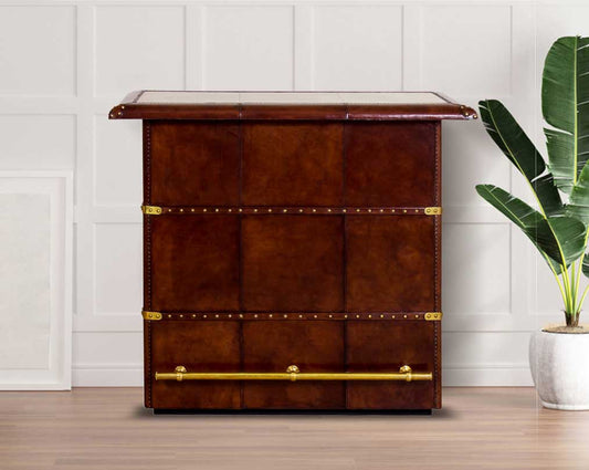 Bar counter in distressed cognac leather with a vintage look with brass hardware and wooden slats. The bar counter has a copper top and comes with storage.