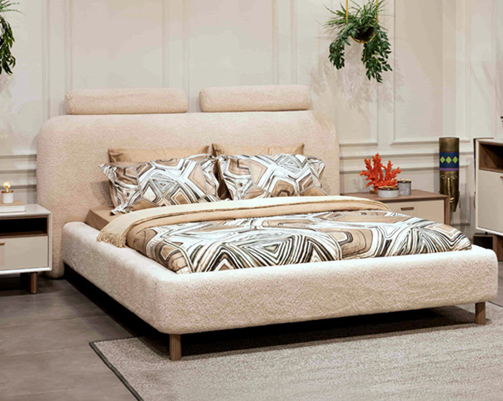 Beige upholstered bed with patterned bedding in a bedroom setting